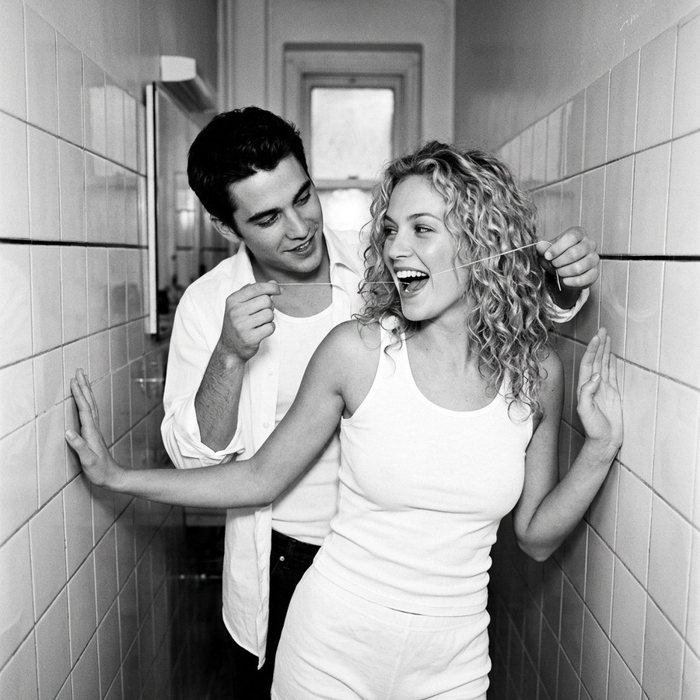A man flosses a laughing woman's teeth in a tiled corridor