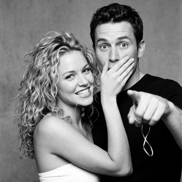 A woman with floss in her smile covers her partner's mouth